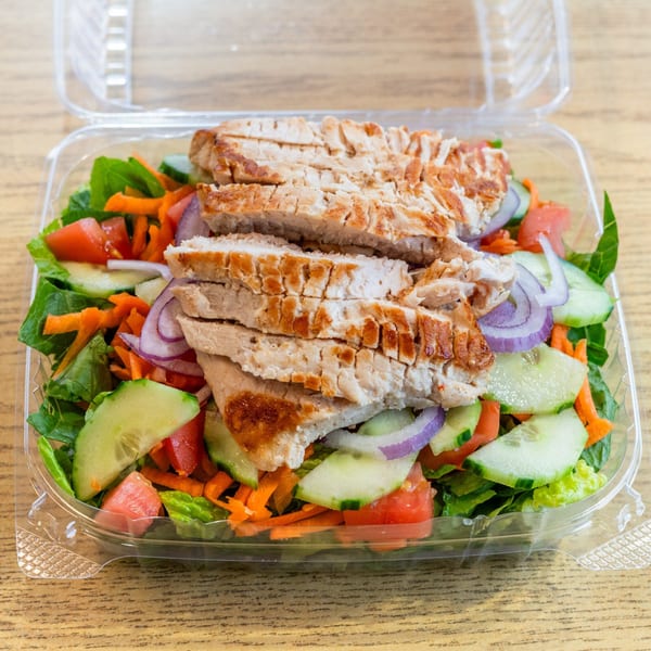 Grilled chicken salad with lettuce, tomatoes, cucumbers, carrots, and red onions in a plastic container.