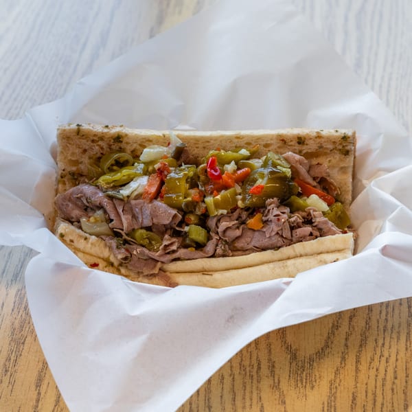 A 5 Points Restaurant Italian beef sandwich with giardiniera, wrapped in white paper on a wooden table.