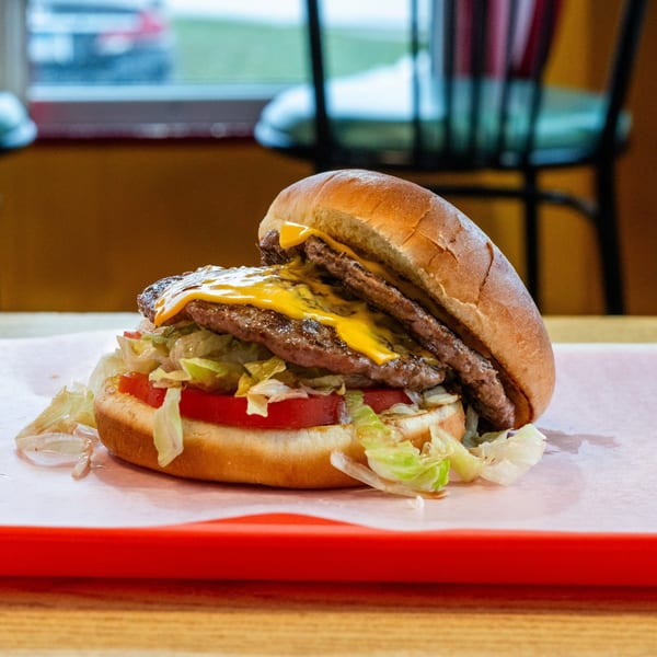 A double cheeseburger with melted cheese, lettuce, and tomato on a bun, served on a red tray.