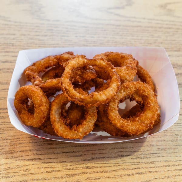 A white paper tray filled with crispy, golden-brown onion rings on a light wooden table.