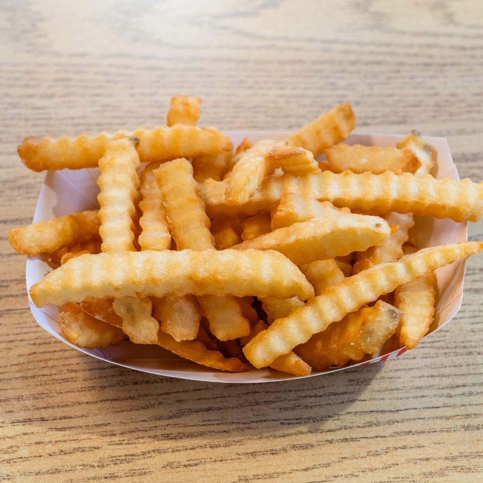 A paper tray filled with golden, crinkle-cut french fries on a light wooden table.