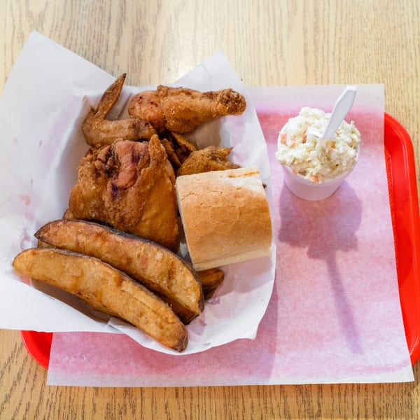 Fried chicken, potato wedges, a bread roll, and coleslaw served on a red tray.