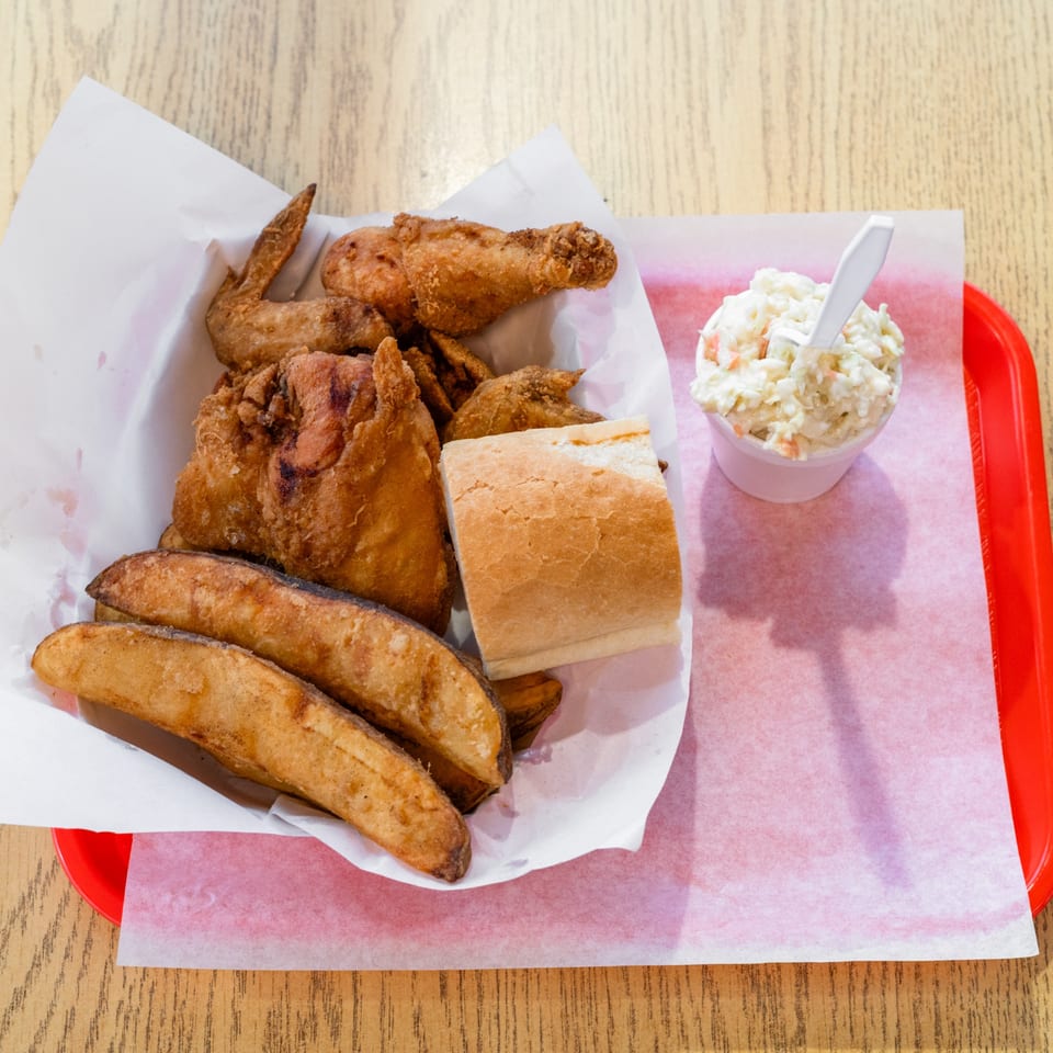 Fried chicken, potato wedges, a bread roll, and coleslaw served on a red tray.
